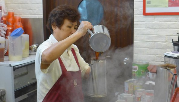 Surrounded by a cloud of steam, a Ya Kun worker makes coffee the traditional way